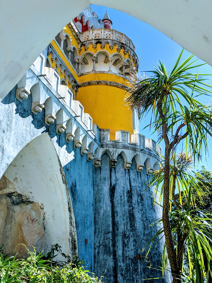 Pena Palace yellow tower and palm tree viewed from below wall