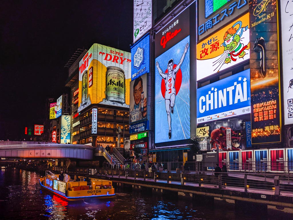 Osaka Dotonbori canal at night with illuminated billboards and boat traveling down waterway.