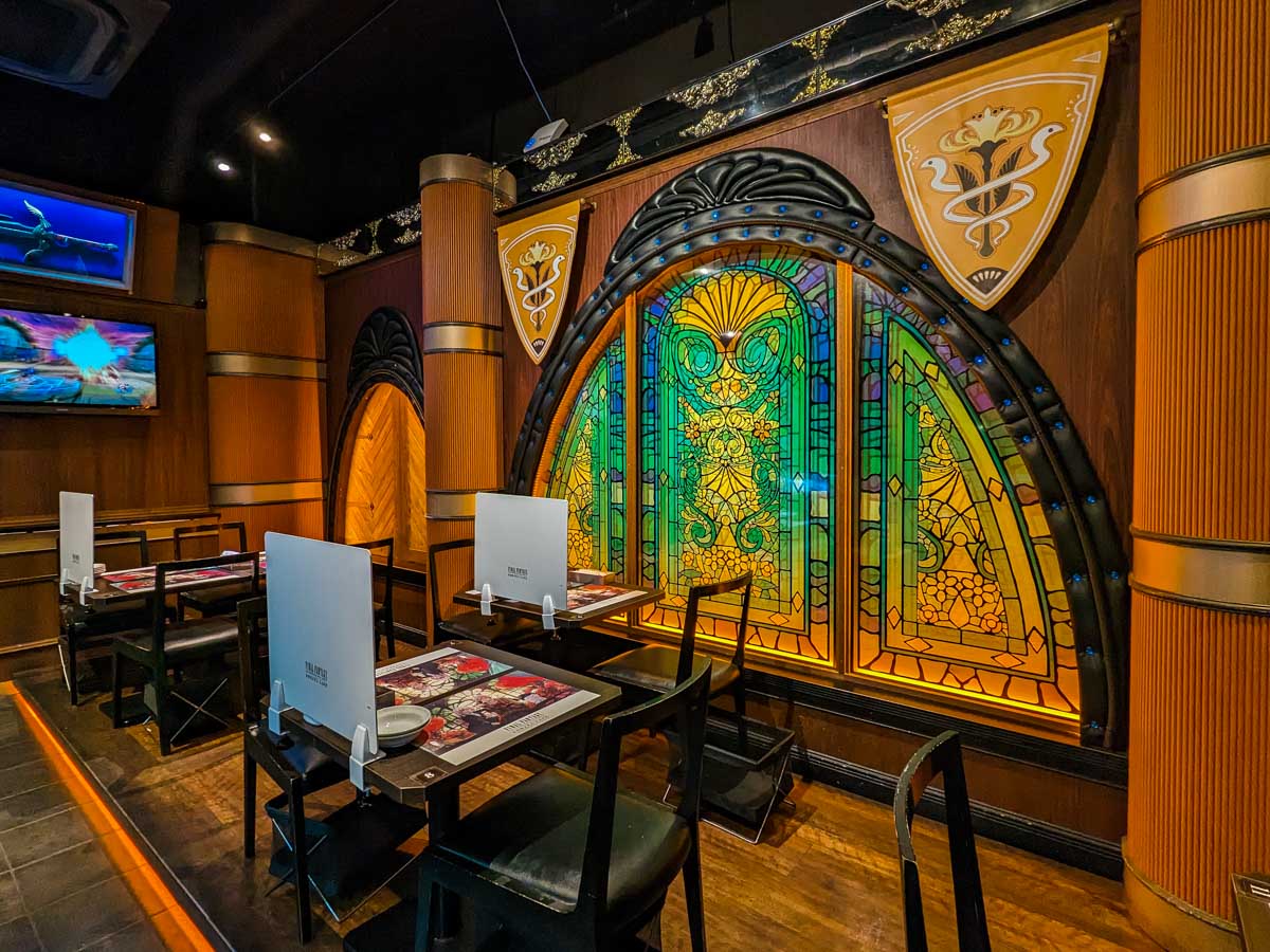 Interior of Eorzea Cafe Tokyo with wooden pillars, tables, and stained glass arch window.