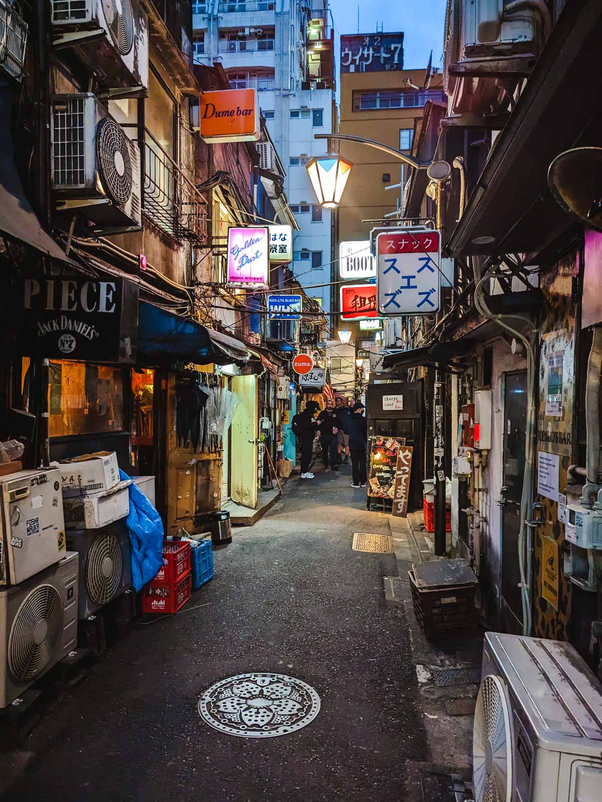 Dark alley of Golden Gai Tokyo lined with air conditioners and bar signs.