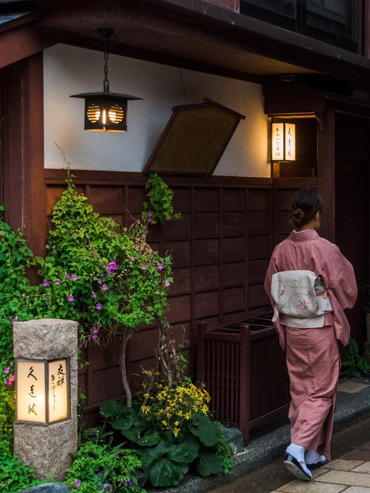 Woman in pink kimono walking in evening under lanterns.