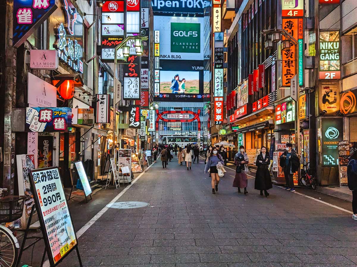 Shinjuku Kabukicho alley at night with illuminated signs and pedestrians.