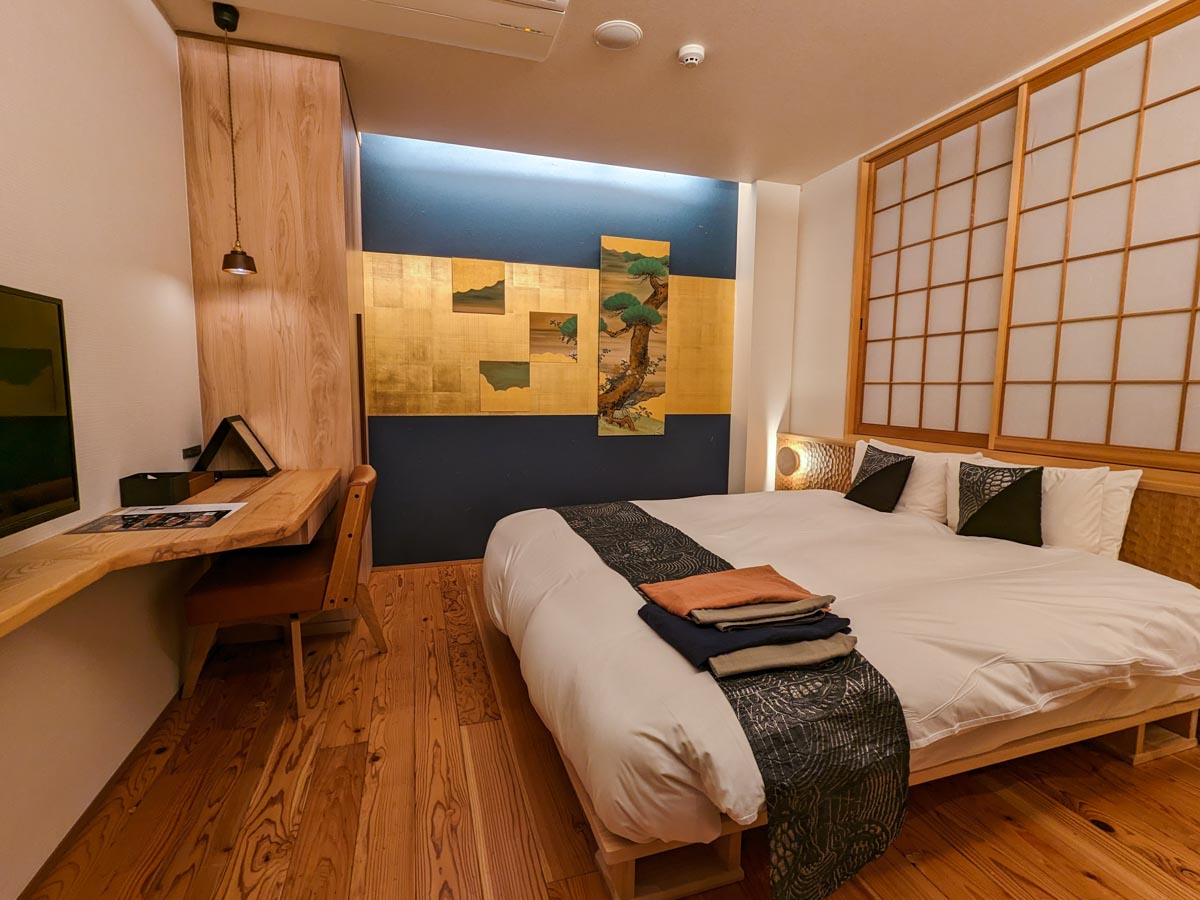 Interior of room at Hotel Kanazawa Zoushi including bed, wall desk, shoji screens, and gold wall art.