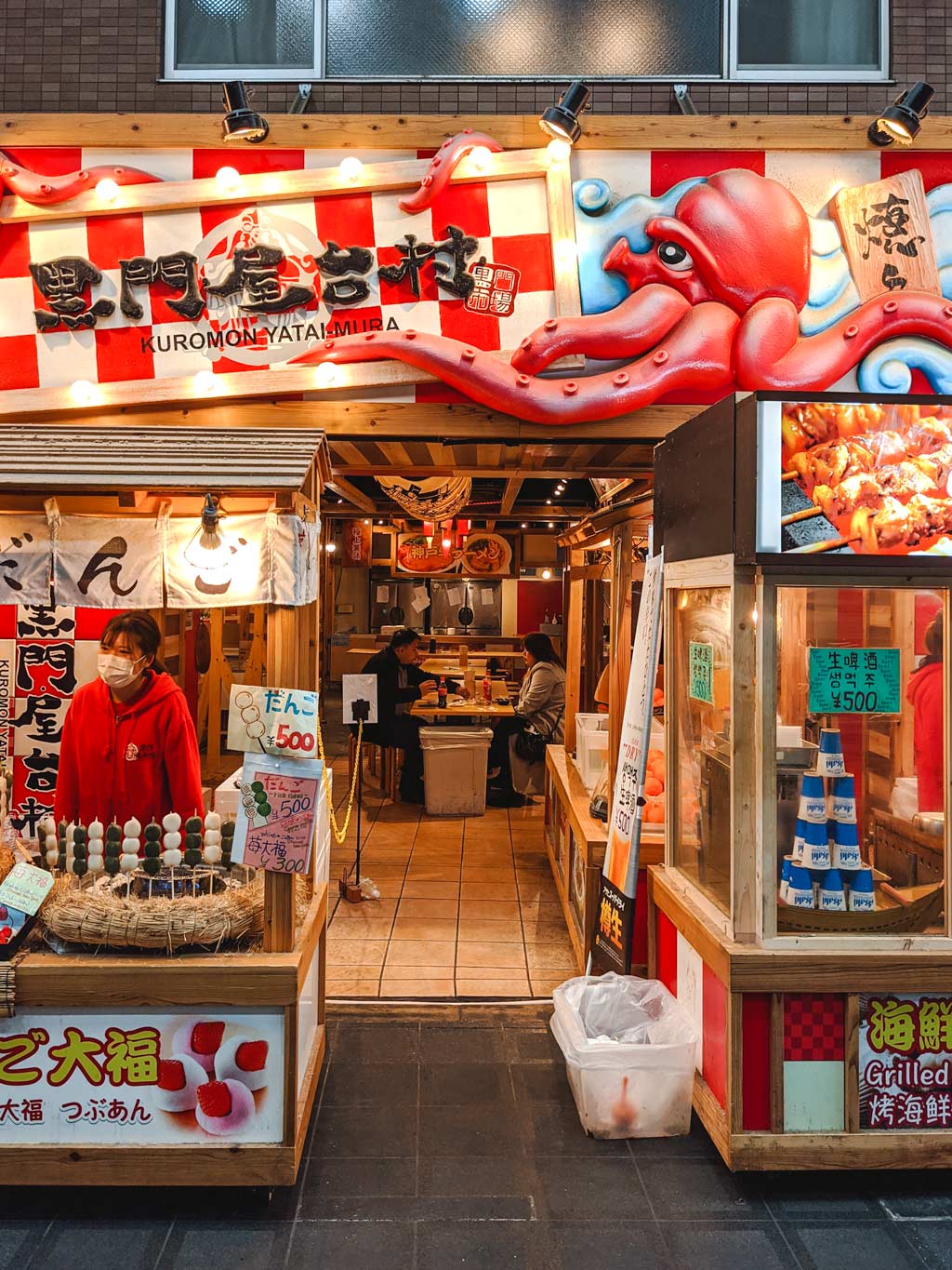 Exterior of takoyaki storefront in Kuromon Market with large cartoon octopus on top.