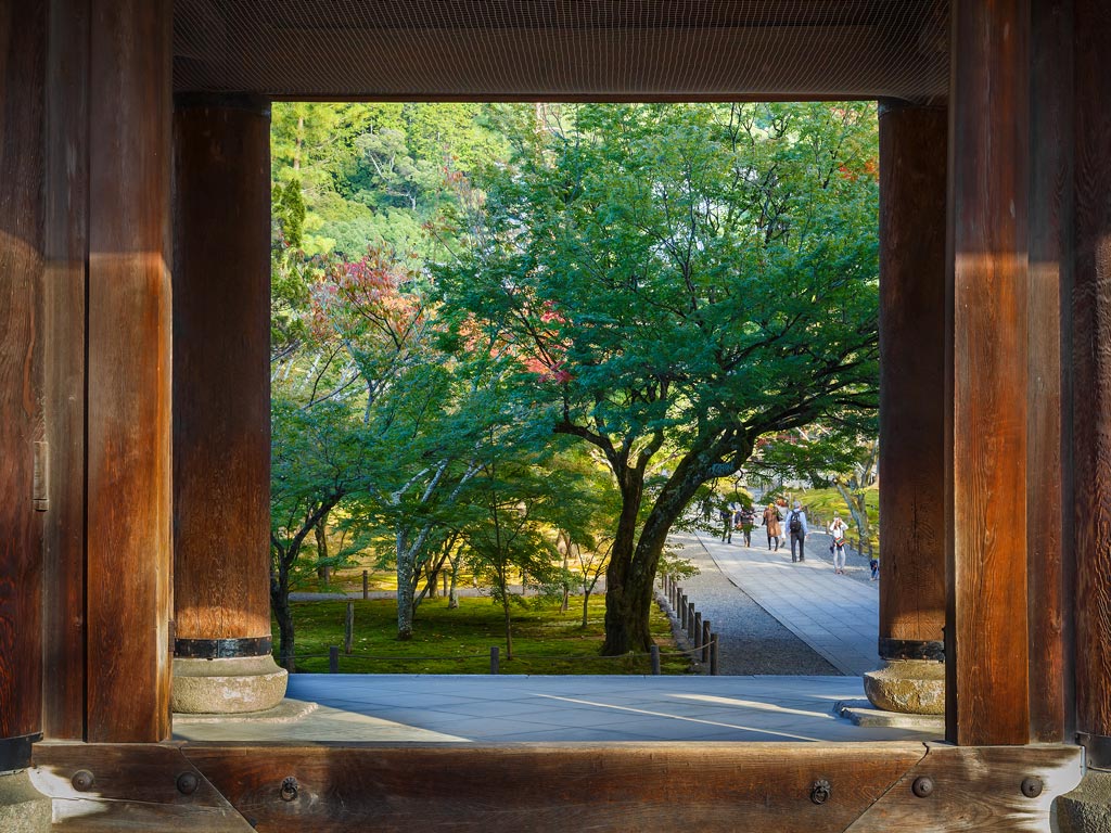 View out of wooden gate towards trees and stone pathway in Nanzenji temple.