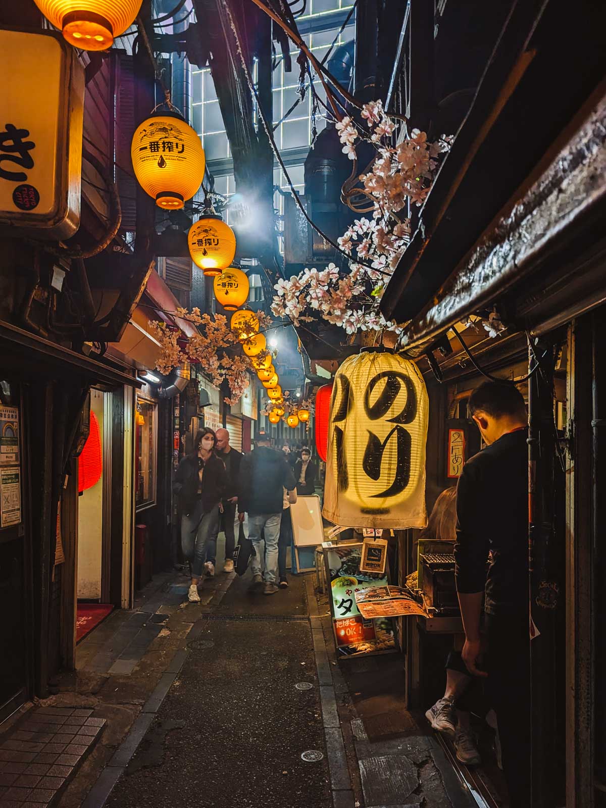 Dark hazy alley of Omoide Yokocho with hanging lanterns and pedestrians.