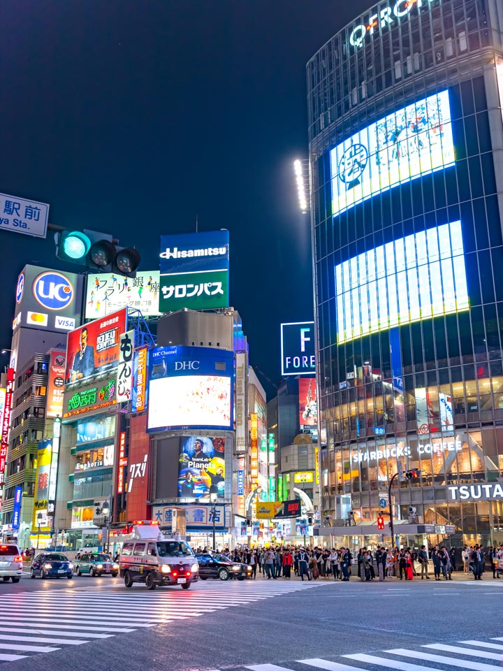 Shibuya Crossing at night with light up signs.