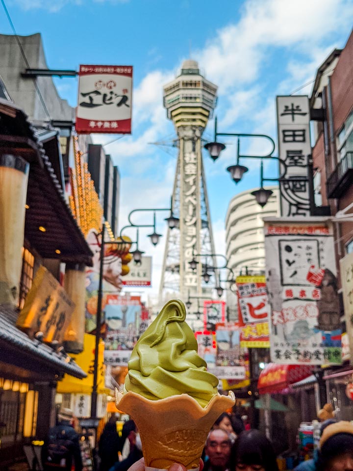 Green ice cream cone with busy Shinsekai street in background.