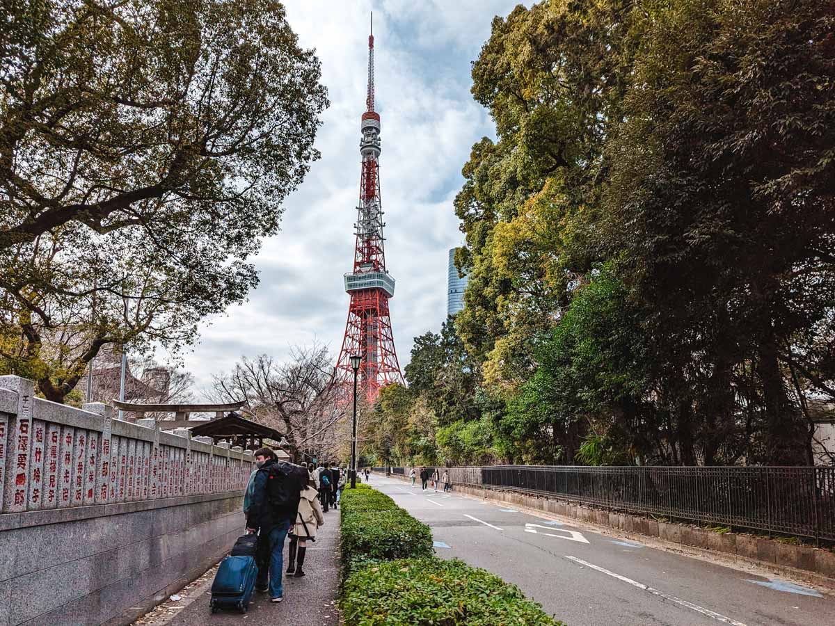 Pedestrians walking down sidewalk towards Tokyo Tower in distance.