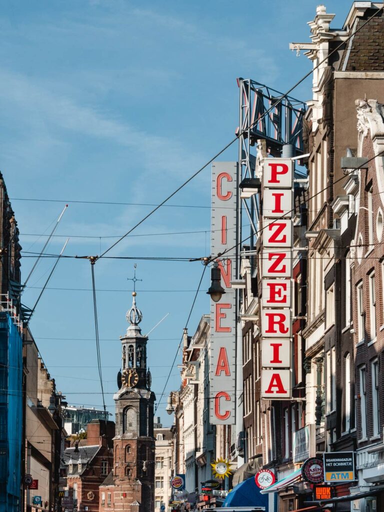 View of Amsterdam old town street with restaurant signs and old clock tower.