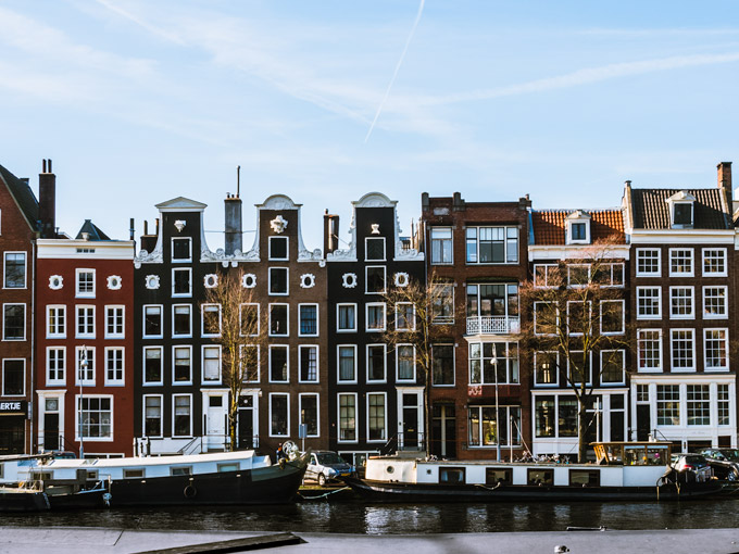 Amsterdam Damrak houses with curving tops and boats on canal.