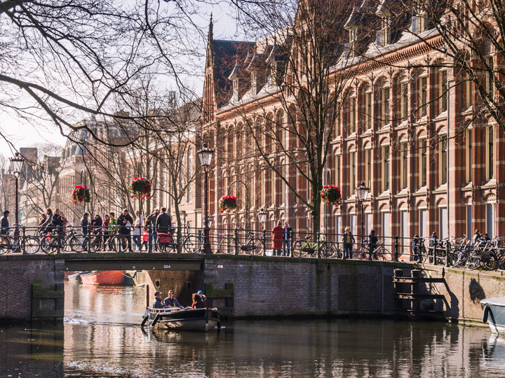 Amsterdam Old Town bridge over canal with pedestrians crossing toward tall brick buildings.