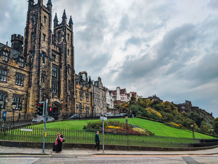 Gothic style mansion behind green lawn against dark cloudy sky in Edinburgh.