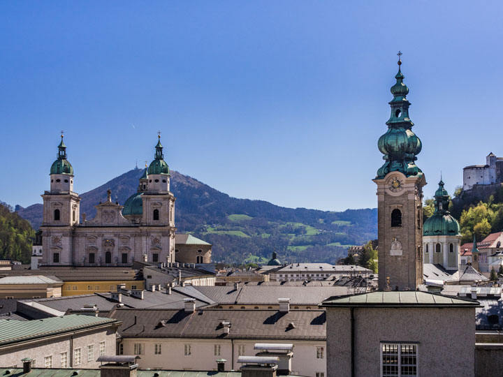 Panoramic view of Salzburg city center including cathedral spires and mountains.