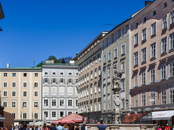 Salzburg city center with pink, white, and yellow buildings and tall water fountain.