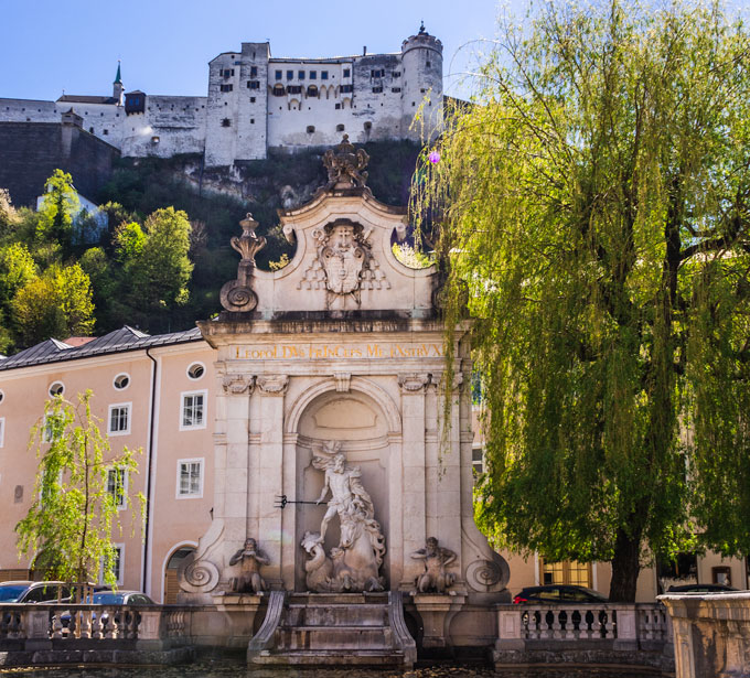 Kapitelschwemme fountain with willow tree and view of Salzburg fortress above.