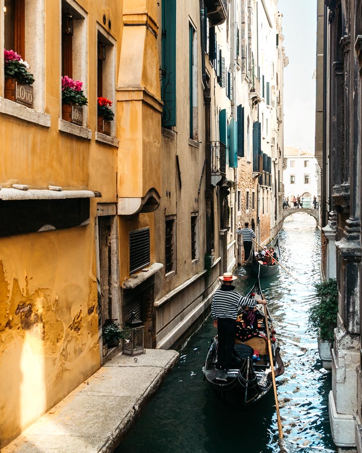 Two gondolas traveling down Venice canal with yellow facade.