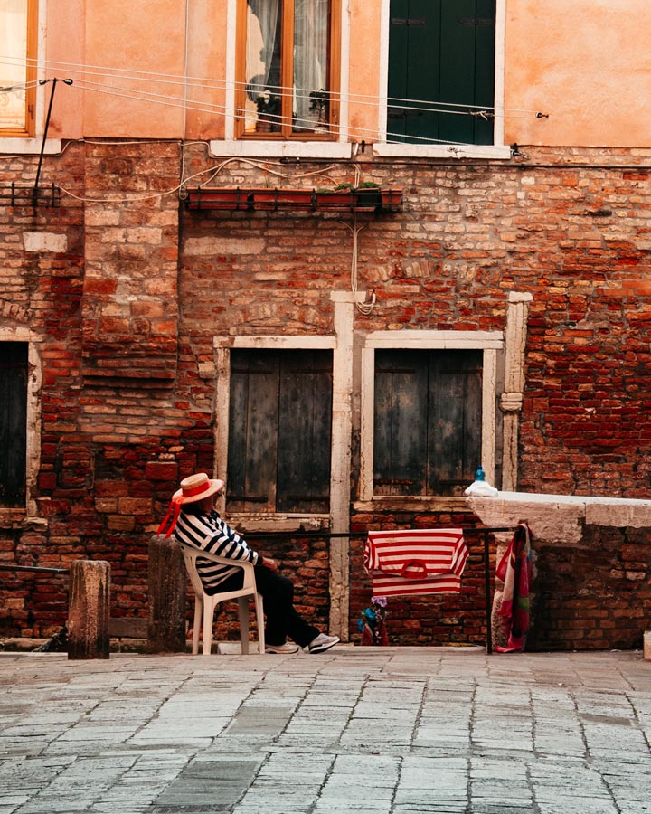Venice gondolier sitting in chair at the end of alley.