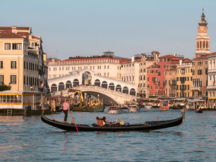 Gondola crossing Grand Canal at sunset in front of Rialto Bridge.