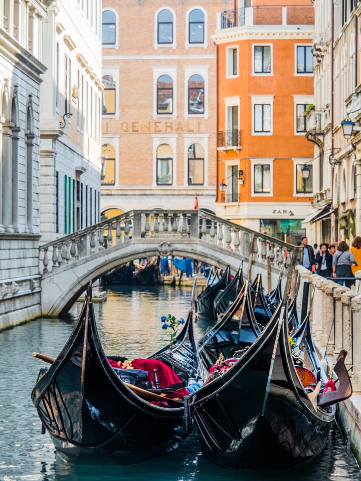 Row of gondolas in Venice canal with bridge and buildings in distance.