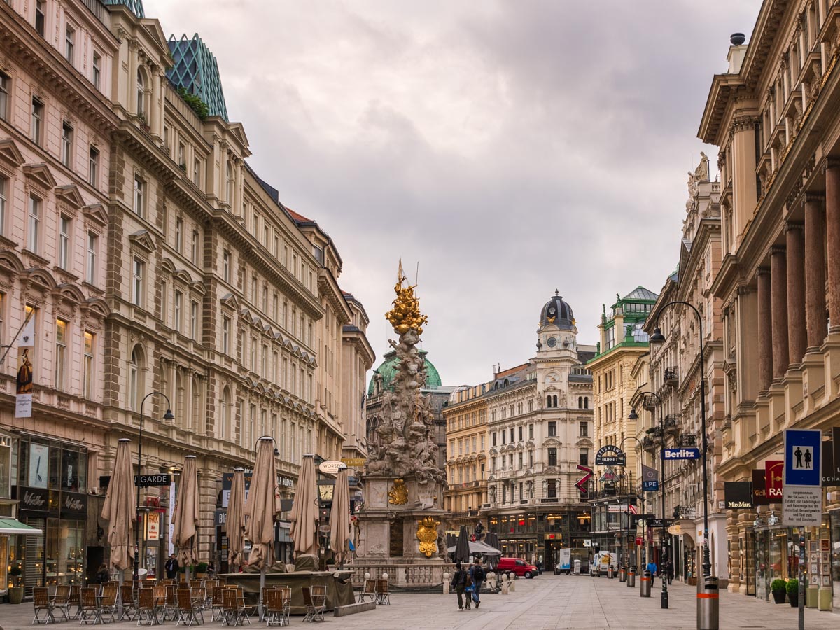 Vienna city center street with large statue, umbrella tables, and pedestrians.