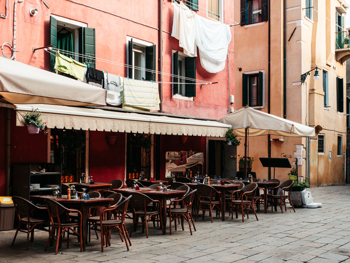 Outdoor cafe in Bologna with wooden tables, pink wall, and hanging laundry