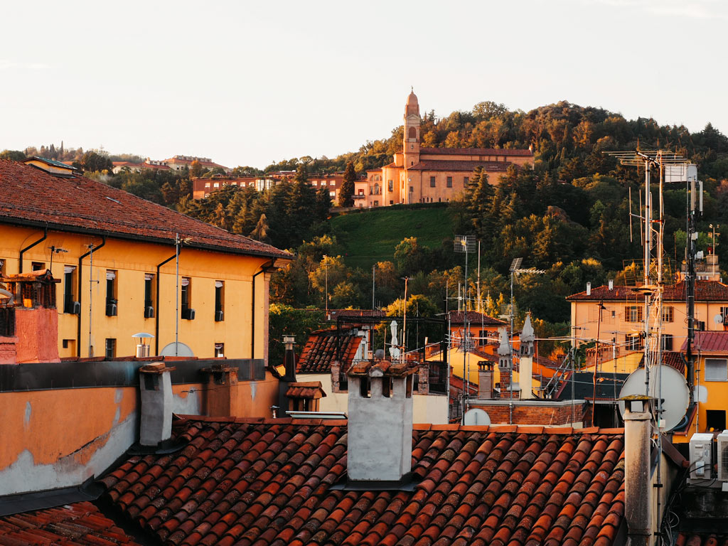 View over Bologna rooftops at sunrise with church on hill in distance.