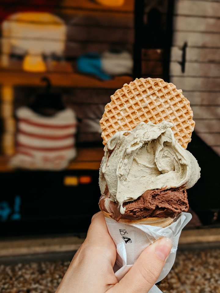 Hand holding istaschio and chocolate gelato cone with waffle circle.