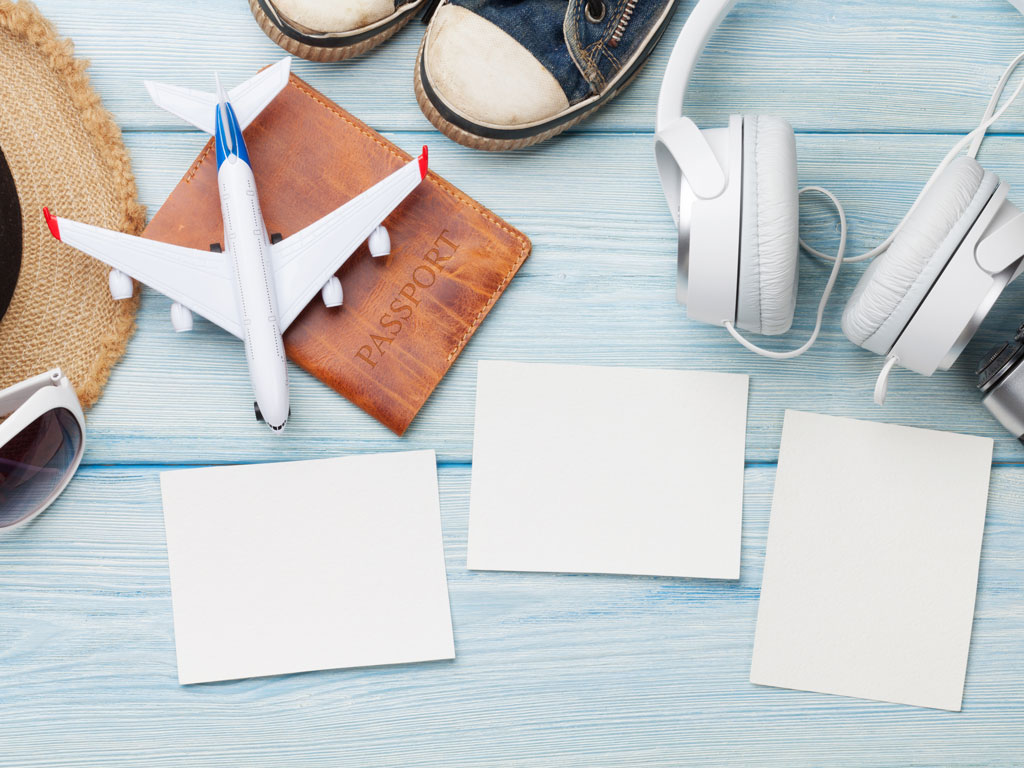 Blue wooden table with 3 white papers, airplane toy, headphones, passport, and shoes on top.