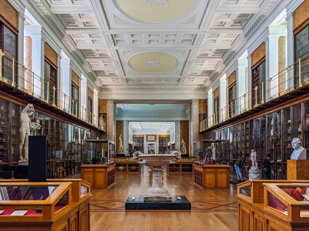 Interior of British Museum's collection room, lined with bookshelves, statues, and display cases.