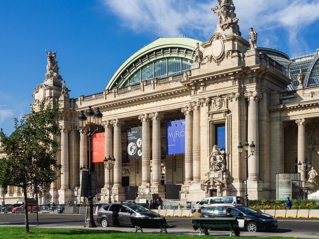 Exterior of Paris Grand Palais with cars parked out front.