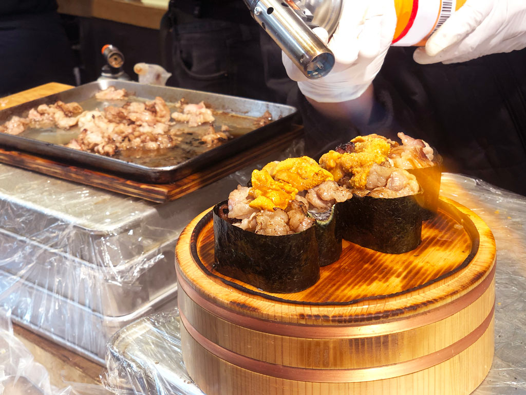 Person blowtorching sushi on top of wooden bowl.