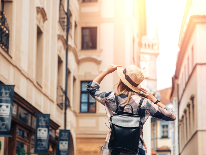 Girl holding straw hat walking down Europe street considering advantages of living abroad.