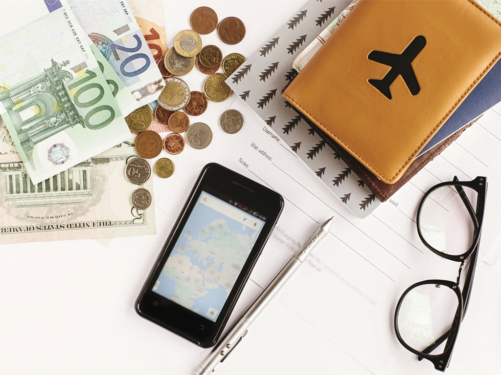 Table with passport holder, glasses, money, and phone showing best budgeting app for expats.