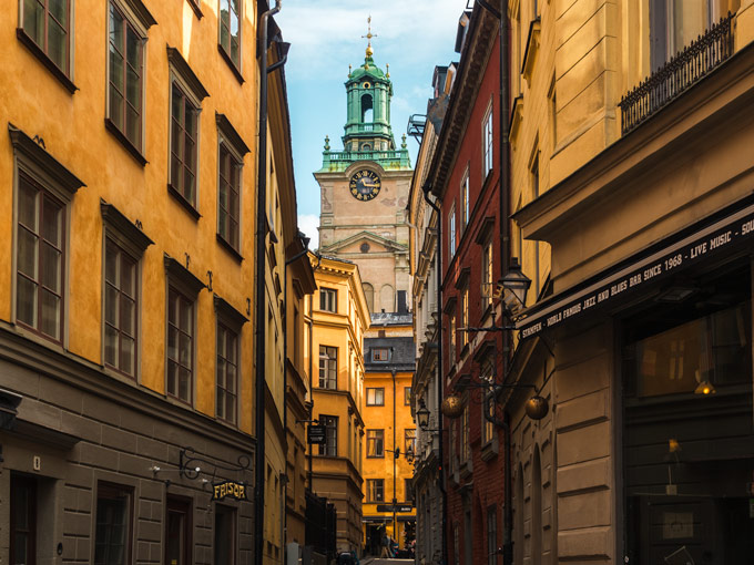 Gamla Stan clock tower viewed from alley with yellow buildings.