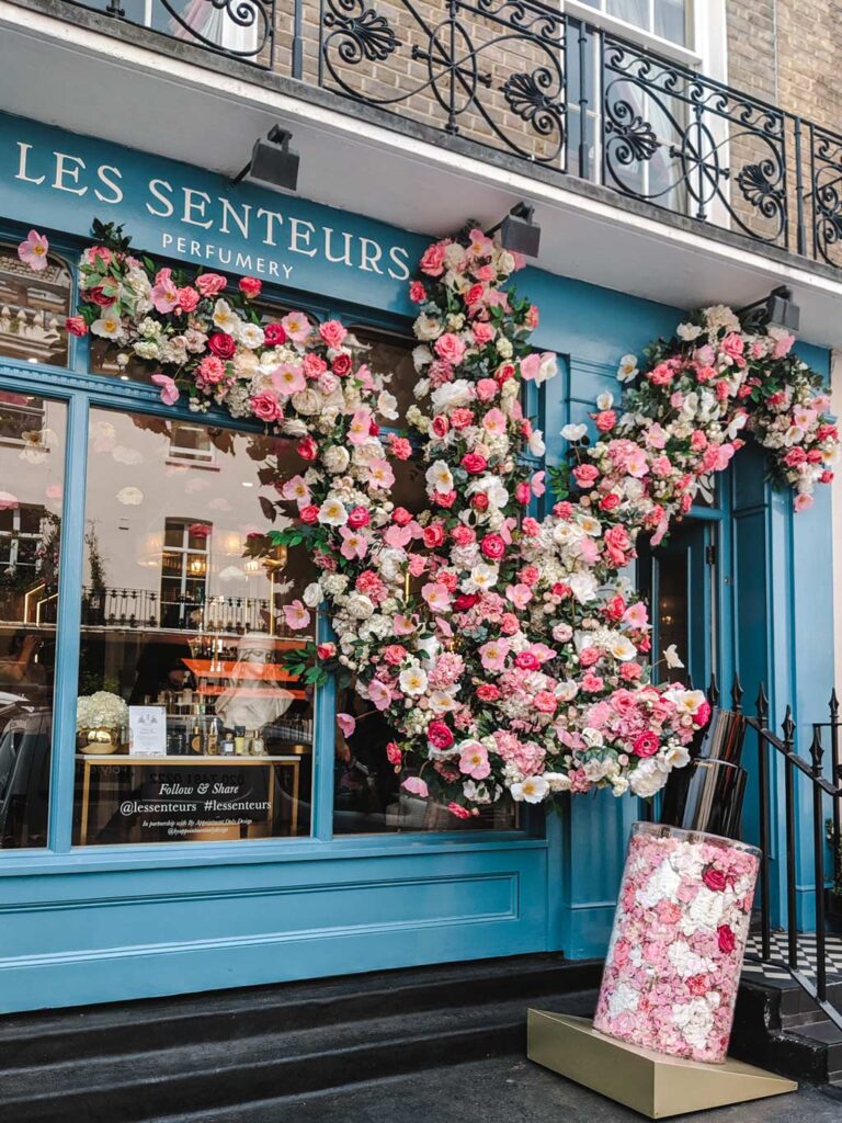 Blue facade of Les Senteurs with flowers and roses on window.