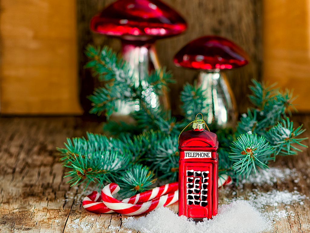 Red phone box ornament in front of pine branch on table.