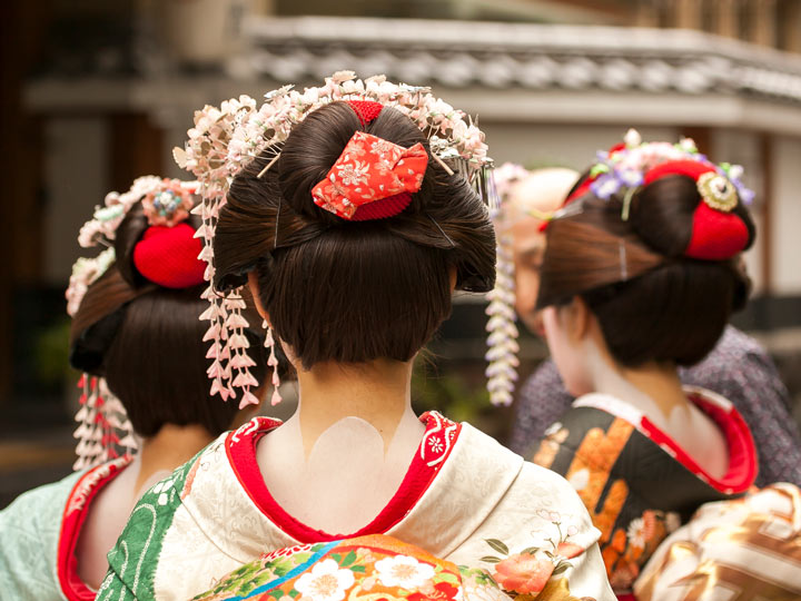 Three geisha walking away with floral hair ornaments kanzashi.