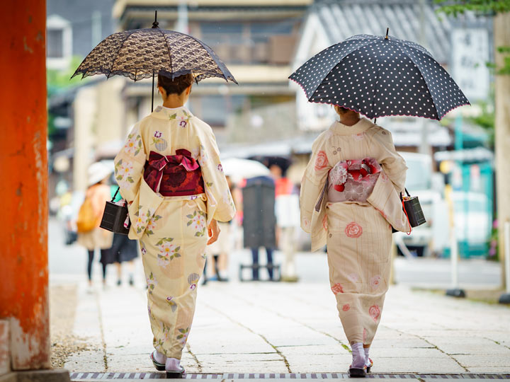 Two women wearing cream colored kimono walking with umbrellas.