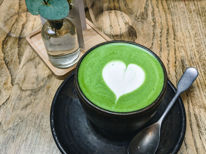 Matcha latte with white heart in black cup.