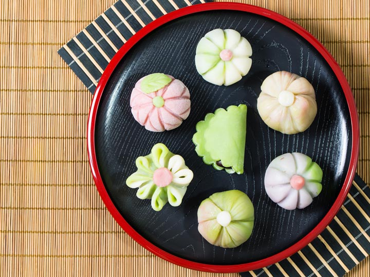 Pink and green flower shaped wagashi on plate with bamboo mat.