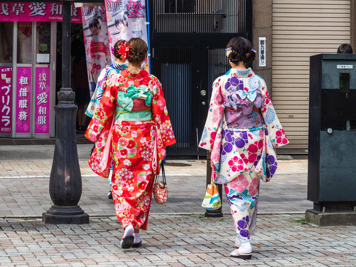 Two girls wearing colorful printed yukata walking away down the street.