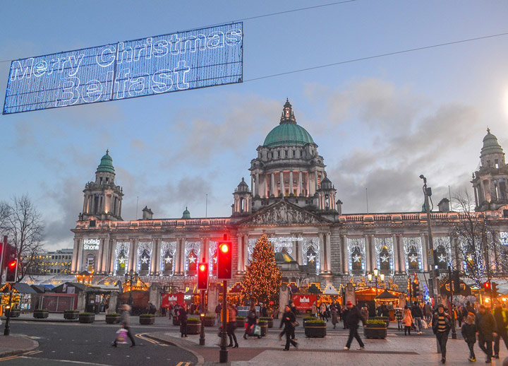 Belfast Christmas market near sunset with illuminated stalls and tree.