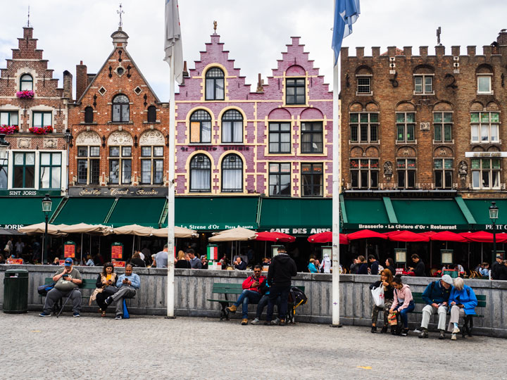 Benches in front of pink and brown old buildings lining market square in Bruges in winter.