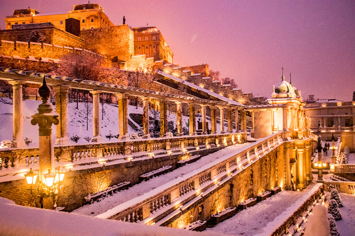 Snow-covered stone facade illuminated at night against pink sky.