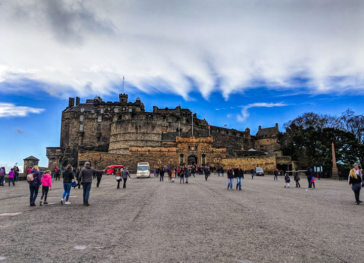 Front view of Edinburgh Castle with tourists under partly cloudy sky.