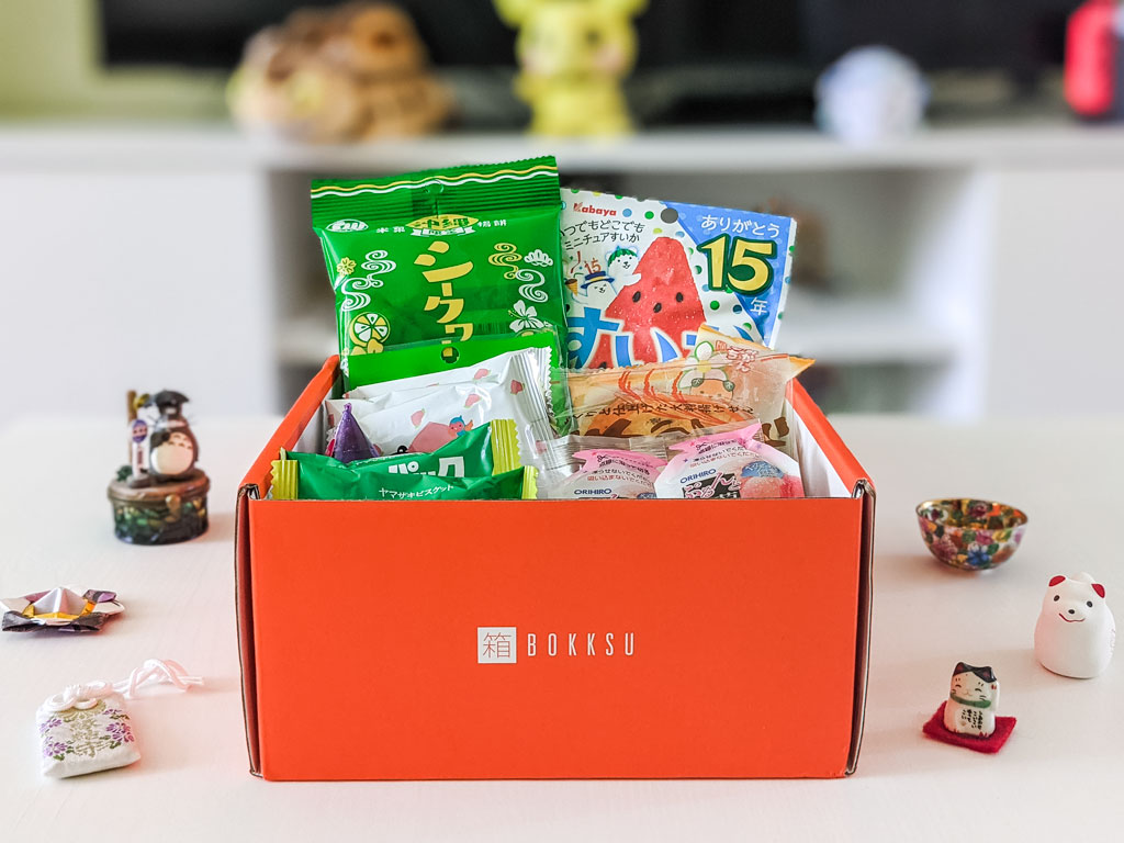 2021 Bokksu review box of Japanese snacks sitting on white table with small figurines and charms.