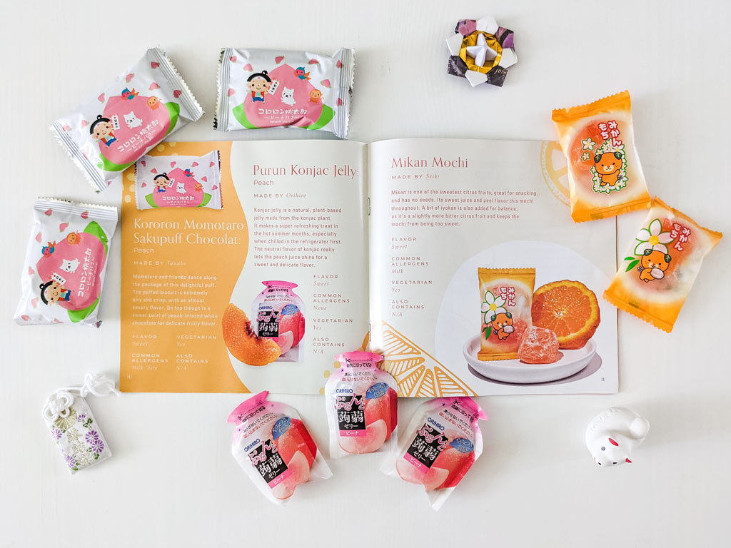 Flat lay of Japanese candy packages on white table, with open Bokksu snack guide in center.