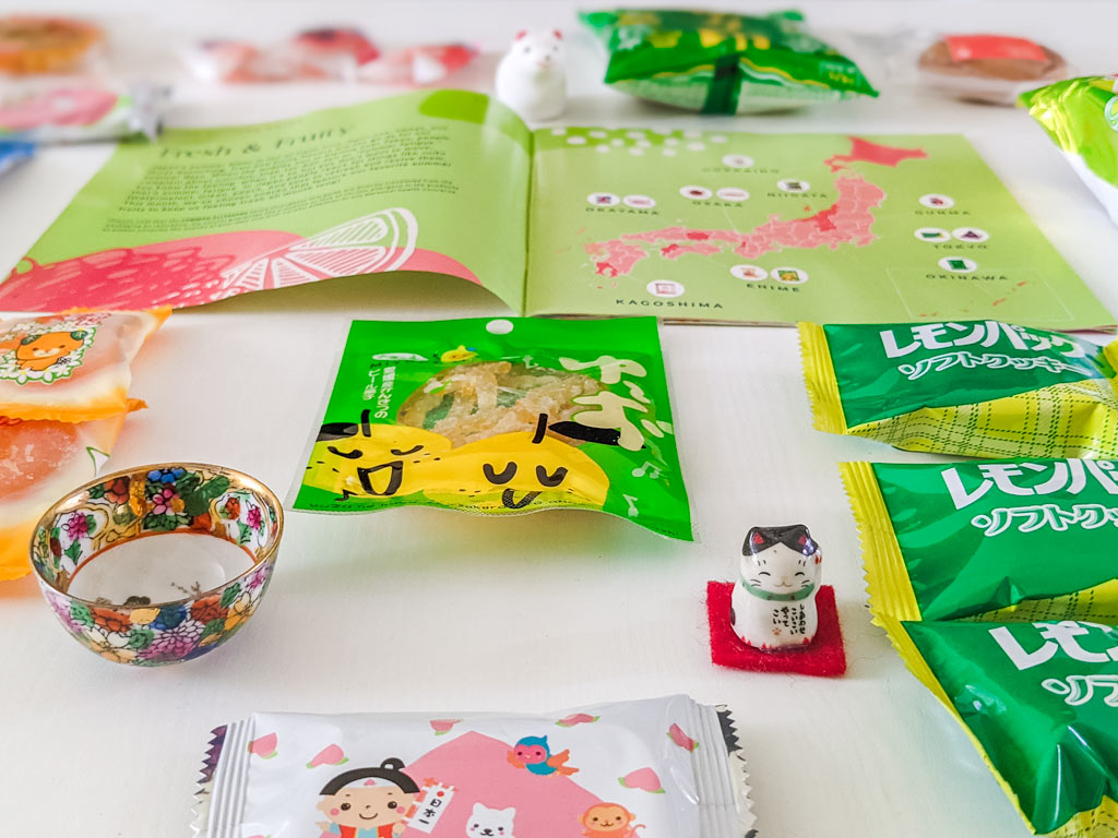 Closeup of lemon peel candy package on table, with map of Japan, cat figurine, and cookie packages  surrounding.