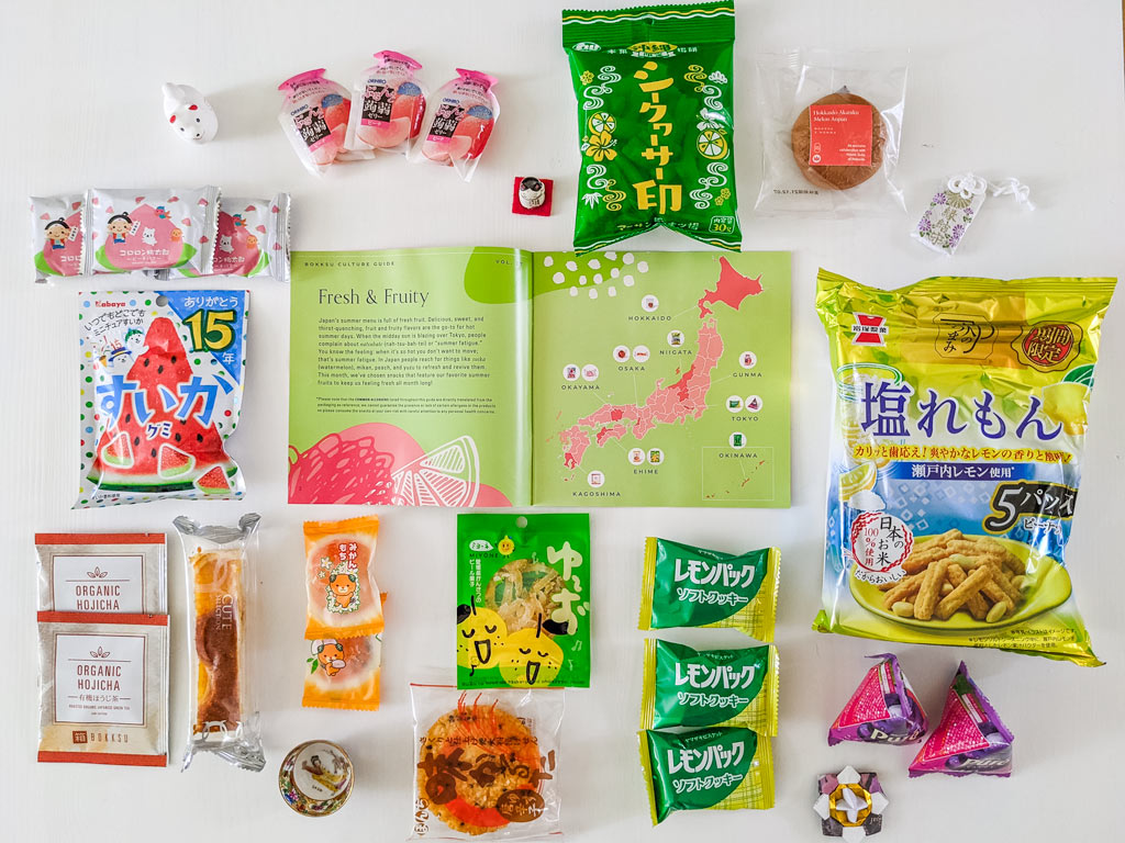 Flat lay of 2021 Bokksu review snack packages found in Summer Fruits box, including rice crackers, orange mochi, and watermelon gummies.